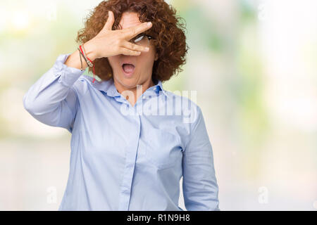 Beautiful middle ager senior businees woman wearing glasses over isolated background peeking in shock covering face and eyes with hand, looking throug Stock Photo