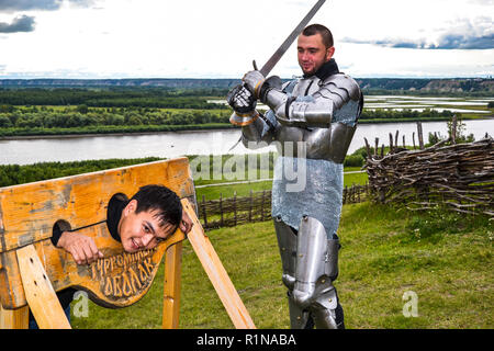 Dramatization penalty in the middle ages. Knight swung his sword at the prisoner. Knightly armor and weapon. Semi - antique photo. Stock Photo