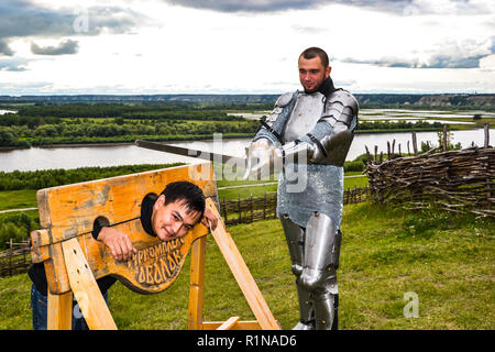 Dramatization penalty in the middle ages. Knight swung his sword at the prisoner. Knightly armor and weapon. Semi - antique photo. Stock Photo