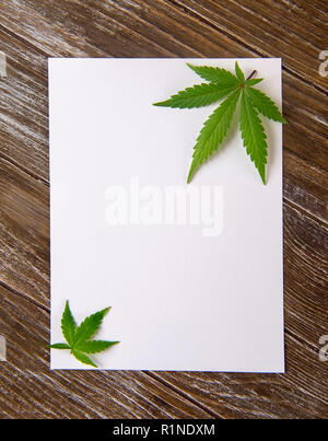 Cannabis leaves isolated over empty white paper on wood background - marijuana card concept Stock Photo
