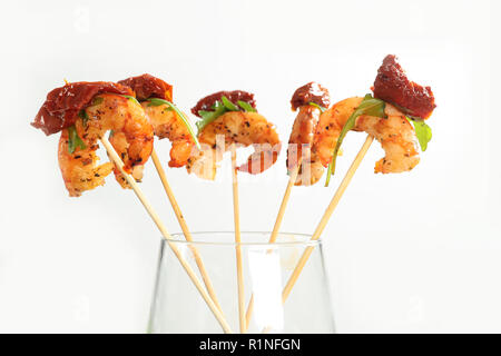 Grilled shrimps with the dried tomato and arugula on sticks, a canape stand in a glass on a white background Stock Photo