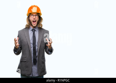 Young handsome architec man with long hair wearing safety helmet over isolated background crazy and mad shouting and yelling with aggressive expressio Stock Photo