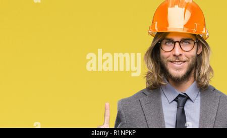 Young handsome architec man with long hair wearing safety helmet over isolated background showing and pointing up with finger number one while smiling Stock Photo