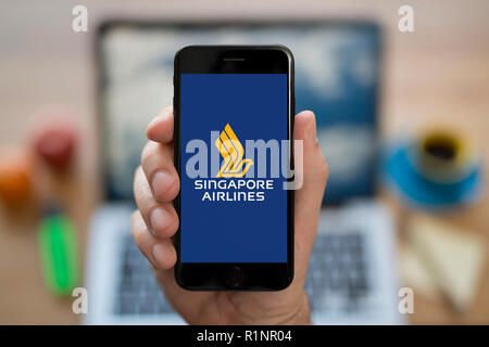 A man looks at his iPhone which displays the Singapore Airlines logo, while sat at his computer desk (Editorial use only). Stock Photo