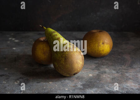 a pear and two rusett apples on a grey textured background with darker lighting creating a moody dark feel to the image Stock Photo