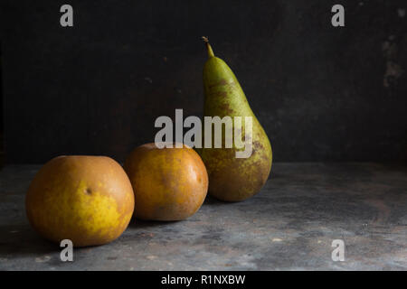 a pear and two russett apples on a grey textured background with darker lighting creating a moody dark feel to the image Stock Photo