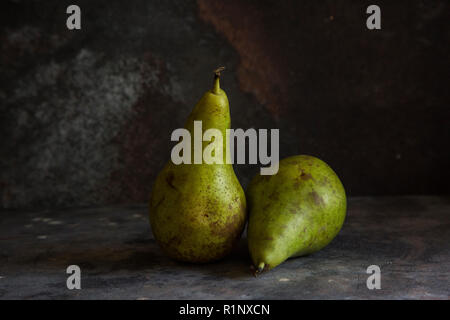 Two whole pears with green and brown skins on a grey textured background and darker lighting, fine art style fruit image Stock Photo