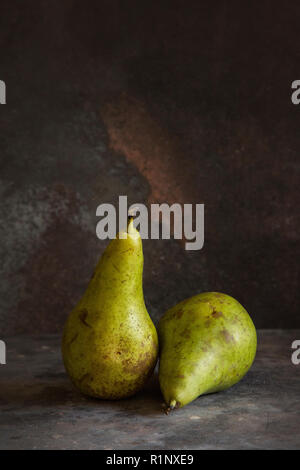 Two whole pears with green and brown skins on a grey textured background and darker lighting, fine art style fruit image Stock Photo