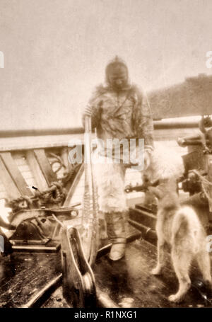 Matt Henson (of Peary's crew) in Arctic costume on deck of the 'Roosevelt' on arrival at Sidney, Nova Scotia - Matthew Henson, full-length portrait, standing, leaning on snowshoes and reaching toward dog. Circa 1906. Matthew A Henson, African American Explorer who was a member of the Peary Expedition that was the first to the North Pole Stock Photo
