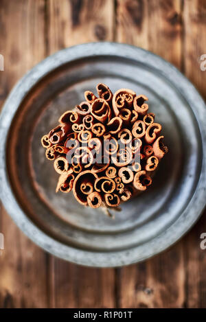 Bunch of Cinnamon sticks on a metallic rustic plate over a wooden table. Stock Photo