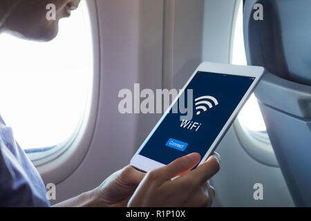 Wifi internet access in airplane during flight, passenger using tablet computer to connect to wireless network technology onboard to read email while  Stock Photo