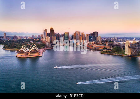 Two speed boats on calm waters of Sydney harbour in view of Circular quay and city CBD high-rise towers and Australian landmarks at sunrise with pink  Stock Photo