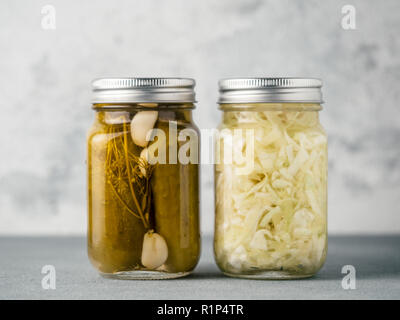 Pickled cucumbers and Sauerkraut on gray background. Perfect homemade marinated cucumbers and pickling cabbage in mason jar at home on table. Stock Photo