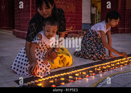 A mother lights candles with her daughter in Mahamuni Image complex, Mandalay, Myanmar. Stock Photo