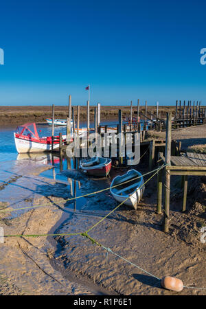 Morston quay and creek in atmospheric North Norfolk. Small boats moored on old wooden jetties and pontoons on a bright autumnal day Stock Photo