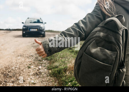Close-up of a tourist girl with a backpack hitch-hiking. She raised her finger up and tried to stop the car to continue her journey. Stock Photo