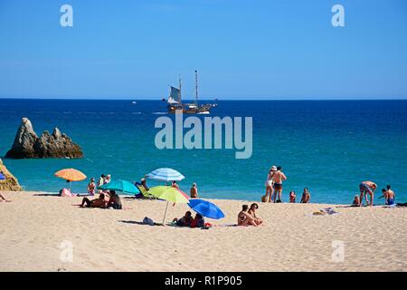Tourists relaxing on the beach and in the sea with a ship in the bay, Praia da Rocha, Portimao, Algarve, Portugal, Europe. Stock Photo