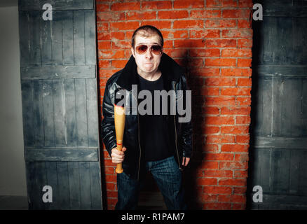 Angry man with bat on brick wall background. Russian gangster 90s Stock Photo