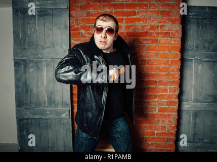Angry man with bat on brick wall background. Russian gangster 90s Stock Photo
