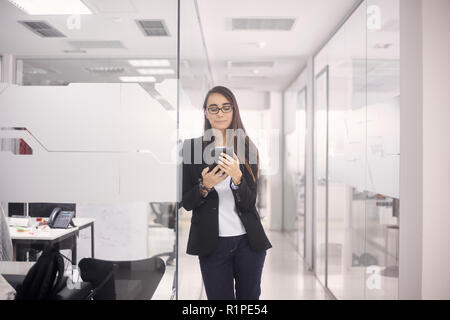 one young woman standing, 20-29 years, smart casual clothes, using tablet in modern interior office. Stock Photo
