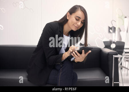 one young woman, 20-29 years old, using tablet, siting in sofa in modern office building. Stock Photo