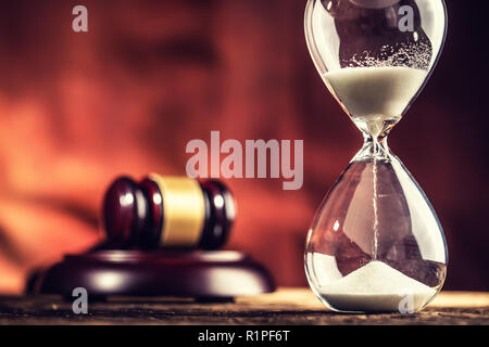 Modern hourglass in running time and justice hammer on wooden table.