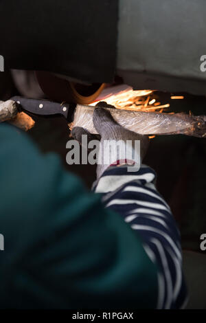 Worker grinding knife in factory setting sanding wheel manufacturing closeup Stock Photo