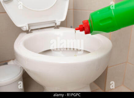 Disinfectant from green bottle being poured in white porcelain toilet bowl as hygiene concept Stock Photo