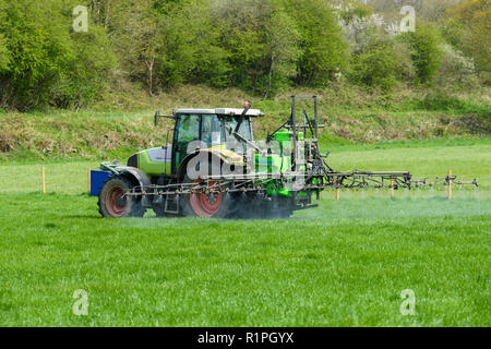 Farmer busy at work on farm, driving tractor spraying crop on farmland, using boom sprayer to distribute chemicals - North Yorkshire, England, UK. Stock Photo