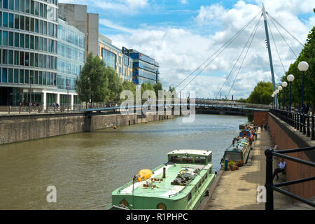 Bristol, UK - 4th August 2016: Moored canal boats and modern office blocks along The Floating Harbour and Temple Back (Temple Quay) regeneration business area in central Bristol City, UK. Workers leave their workplaces during a sunny summertime lunch break. Stock Photo