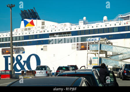 Calais, France - April 11th, 2017: A cross-channel P&O ferry docks beyond a line or cars waiting to board their ship at the Port of Calais, France on a sunny spring afternoon. Calais is the largest port in France for passenger traffic. Stock Photo