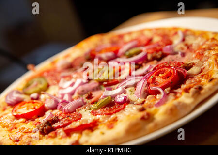 Spicy fresh thin crust pizza - jalepenos, spicy beef, pepperoni, red onions, close up food photography with out of focus elements Stock Photo