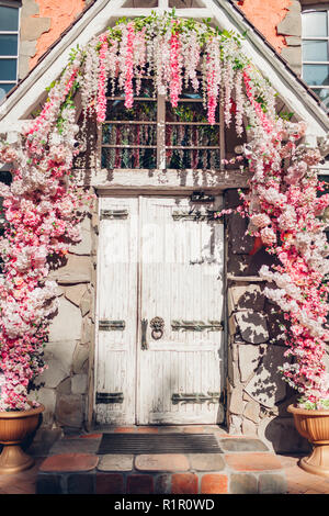 Old wooden door decorated with white and pink flowers. Exterior design. Vintage retro cafe entrance. Stock Photo