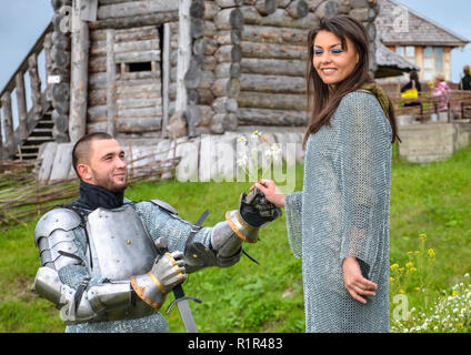 A knight in armor gives chamomile to his lady heart. Stock Photo