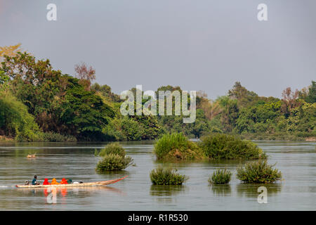 Don Det, Laos - April 22, 2018: Wooden longboat navigating the mekong river surrounded by forest near the Cambodian border Stock Photo
