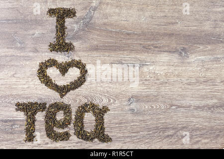 Words I love tea made of green tea leaves on wood background. Text on the left Stock Photo