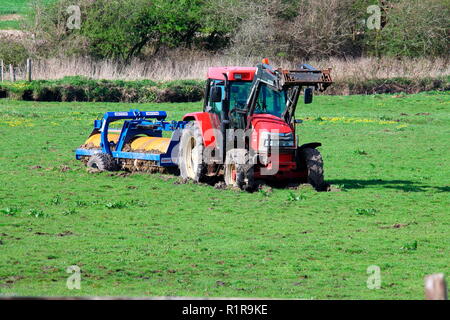 Nice new red tractor towing a very heavy grass roller stranded deeply in the middle of a very muddy field and sinking. Stock Photo