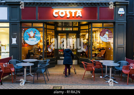 A woman enters a branch of Costa coffee in King's Lynn High Street at dusk. Stock Photo