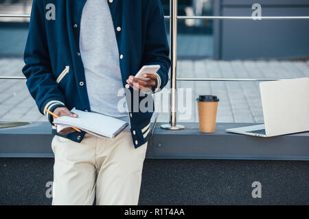 cropped view of freelancer with documents, smartphone, laptop and coffee to go in city Stock Photo