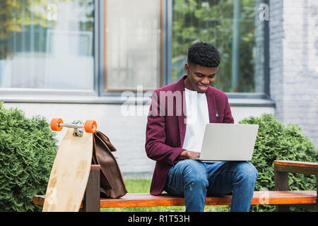 smiling young african american student using laptop on street Stock Photo