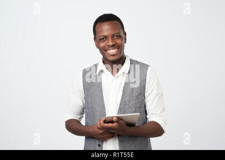 Using modern technologies. Handsome young african man in shirt and vest with digital tablet and smiling while standing against grey background Stock Photo