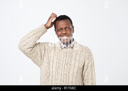 Young african man in sweater thinking scratching head on white background. How is it supposed to be done concept Stock Photo