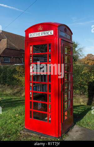 Old-fashioned red telephone box or kiosk on The Street near the village hall in the village of Rotherwick in Hampshire, UK, now used as a library Stock Photo