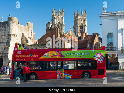 An electric open topped tourist bus parked in St Leonards Place in York city centre, with Bootham Bar and York Minster in the background, North Yorksh Stock Photo