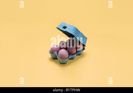 Half dozen free range organic brown eggs in open carton.  Six brown eggs in open crate container on bright pastel yellow background Stock Photo