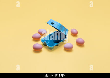 Half dozen free range organic brown eggs lying around the carton.  Six brown eggs scattered around crate container on bright pastel yellow background Stock Photo