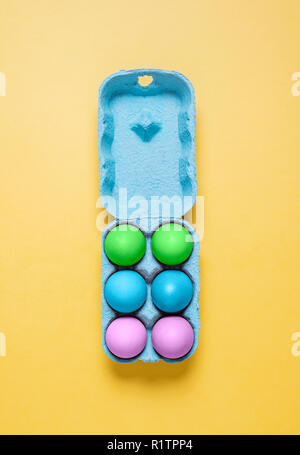 Half ozen pastel dyed Easter eggs in carton on yellow.  Six painted easter eggs in crate container on a bright pastel yellow background Stock Photo