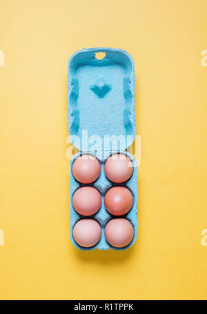 Top view of half dozen free range organic brown eggs in carton.  Six brown eggs in crate container on a bright pastel yellow background Stock Photo