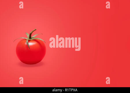 Single ripe red cherry tomato offset to the left on a matching red background with copy space and room for text on a horizontal image Stock Photo