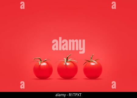 Three ripe red cherry tomatoes in a row on a matching red background positioned on the bottom of the frame with copy space and room for text Stock Photo